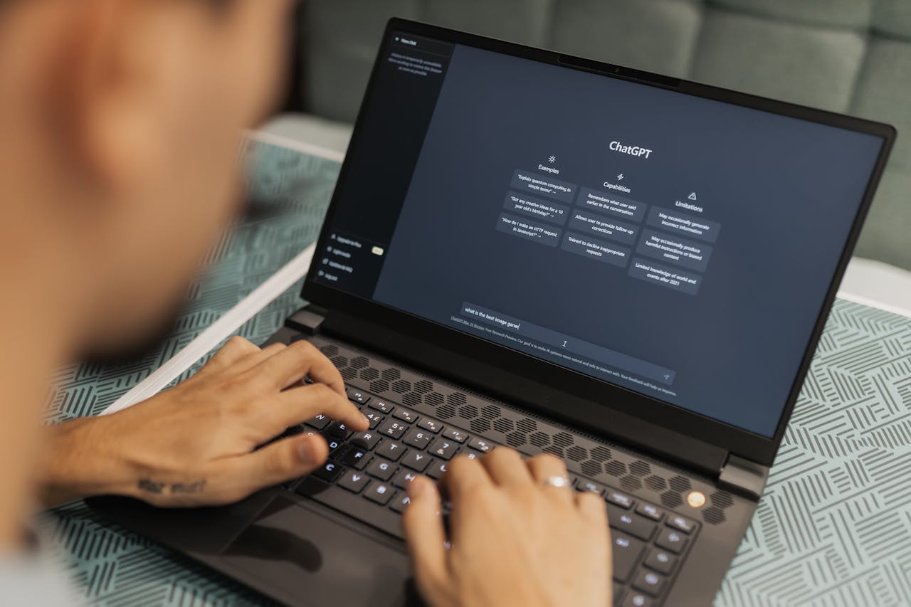 team-02 Close-up of a person typing on a laptop displaying the ChatGPT interface, emphasizing modern technology use.